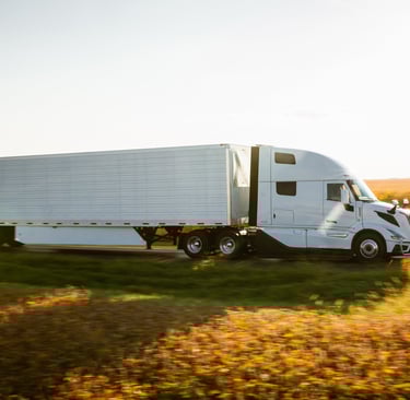 White semi-truck with a long trailer drives on a rural highway during golden hour, transporting goods.
