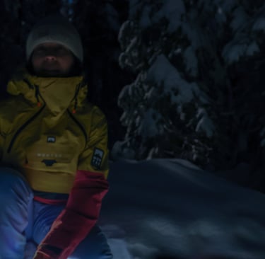 A person sitting in a snowy forest at night, lit by full moonlight.
