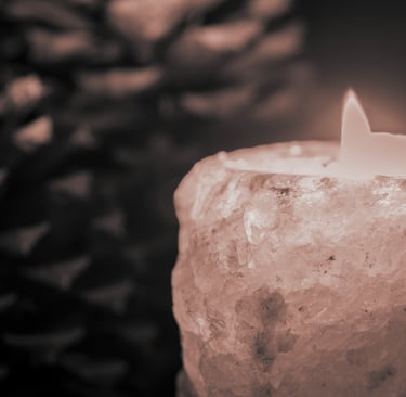 Close-up of a lit candle in a crystal holder with blurred pinecone in background
