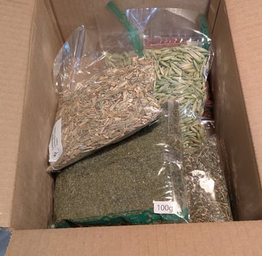 Open cardboard box containing several plastic bags filled with dried herbs and tea ingredients.