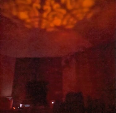 Lit candle lantern casting patterned light onto a wall in a dark room.