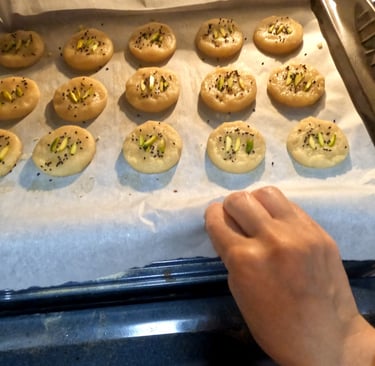 Round cookies with pistachios and seeds on a tray being placed into the oven