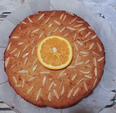 An almond orange cake topped with sliced almonds and an orange slice, cooling on a rack.