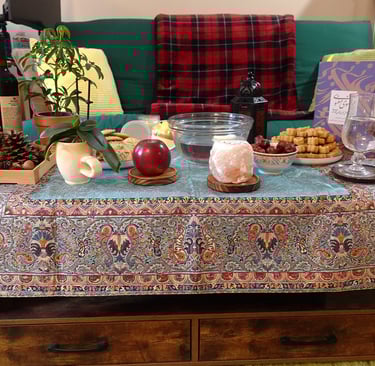 Haft-seen table with candles, apple, dates, cookies, book, and plants on a coffee table