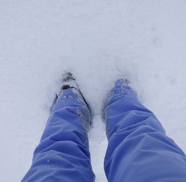 Person standing in deep snow, looking down at their legs and boots partially covered by snow.