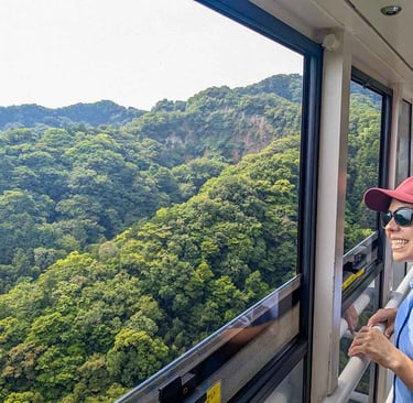 Woman smiling from a cable car descending toward a quiet village surrounded by lush green hills in Shizuoka, Japan.