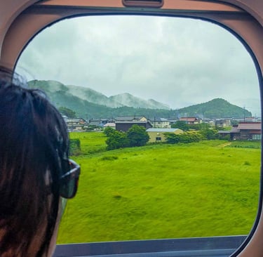 View from the Hikari Shinkansen window showing misty countryside and green fields on the journey to Kyoto, Japan.