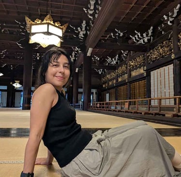Woman sitting inside Nishi Hongan-ji Temple in Kyoto, surrounded by wooden pillars and tatami flooring.
