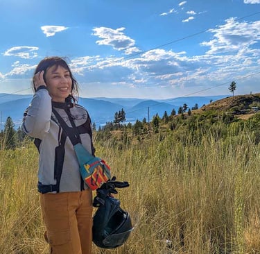 Woman standing beside a motorcycle helmet overlooking mountains and grasslands near Penticton, British Columbia.