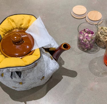 Teapot in a fabric warmer with rose buds, cardamom, and saffron on a kitchen counter.