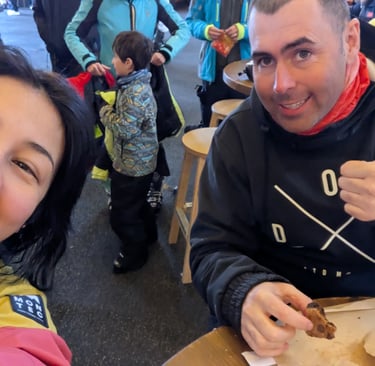 Two people sitting at a table indoors, one giving a thumbs up and holding a cookie.