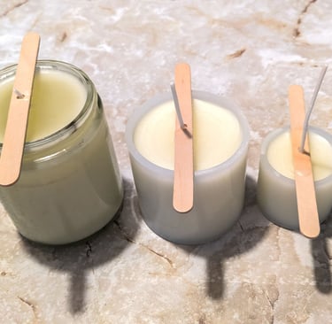 Three homemade candles cooling in glass containers on a marble surface with wooden sticks holding th