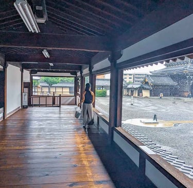 Woman walking through a covered corridor at Nishi Hongan-ji Temple while rain falls over the temple grounds in Kyoto, Japan.