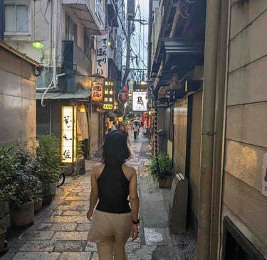 Woman walking through a narrow food street lined with restaurants and lanterns in Osaka, Japan.