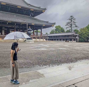 Woman holding an umbrella in the courtyard of Nishi Hongan-ji Temple during a rainy afternoon in Kyoto, Japan.