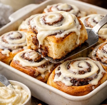 Freshly baked homemade cinnamon rolls with cream cheese frosting being lifted from a baking dish.