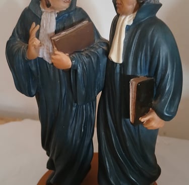 Statue vintage de deux avocats en robe traditionnelle et chapeau portant des dossiers juridiques.