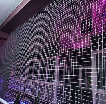 Evening shot of a balcony with pigeon netting, softly lit by warm indoor lights.