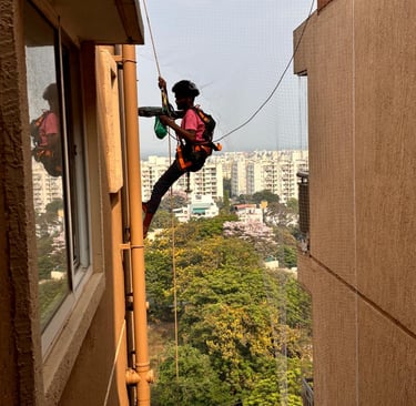 A technician carefully installing pigeon nets on a balcony in Bellandur, Bangalore.