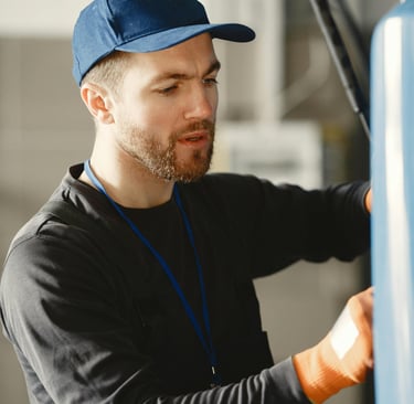Professional mechanic wearing a blue cap and work gloves repairing a vehicle in an auto body shop.