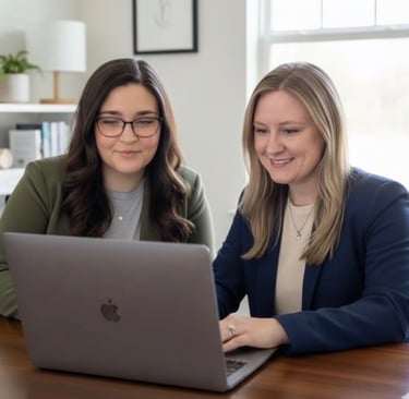 Two professional women collaborating on a laptop in a bright modern office setting.