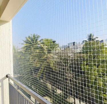 Wide shot of a balcony fully covered with safety netting overlooking a green neighborhood in Adyar.