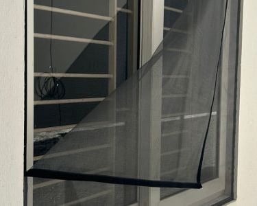 Close-up of a freshly installed mosquito net on a balcony window in Bangalore, sunlight filtering th