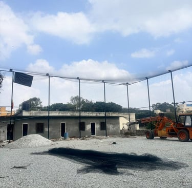 Evening view of a cricket ground illuminated by floodlights, showcasing the installed boundary nets