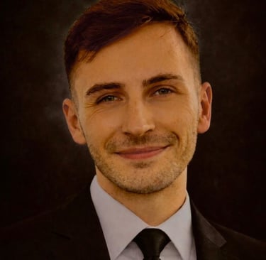A smiling Bradley in a black suit and tie against a dark background.