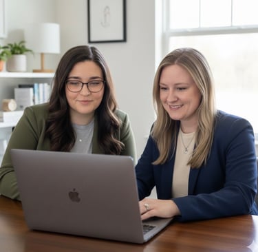 two women sitting at a table with a laptop
