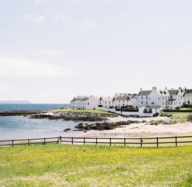 White coastal houses overlooking a sandy beach and rocky shoreline in a scenic Scottish village.