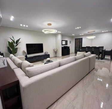 Modern open-plan living room with a large sectional sofa, flat-screen TV, and dining area.