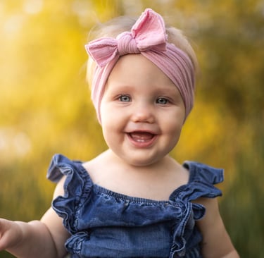 Smiling baby wearing a pink bow during an outdoor portrait session.