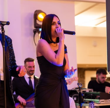 Female lead singer in a black dress performing with a live wedding band at a gala event.