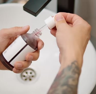 Hands holding a glass dropper bottle with liquid, removing the dropper over a bathroom sink.