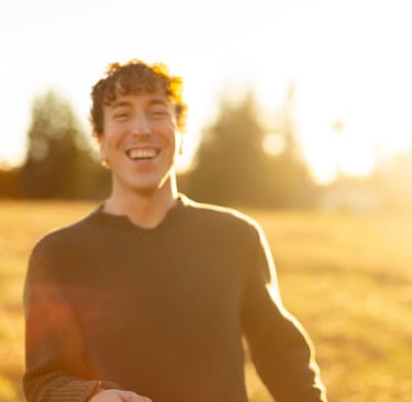 A happy man with curly hair laughing in a golden sunlit field during sunset.