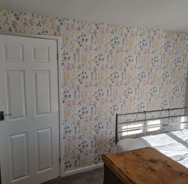 Freshly wallpapered wall of a bedroom, with various plants on a white/cream background.