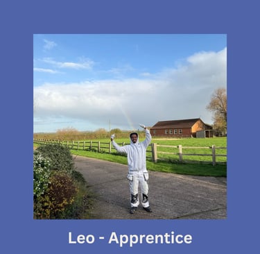 Portrait of Leo, an apprentice painter, standing on a driveway and gesturing towards a rainbow.