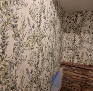 Top of a staircase with pale, vine-like wallpapered walls leading downstairs, in a residential home.