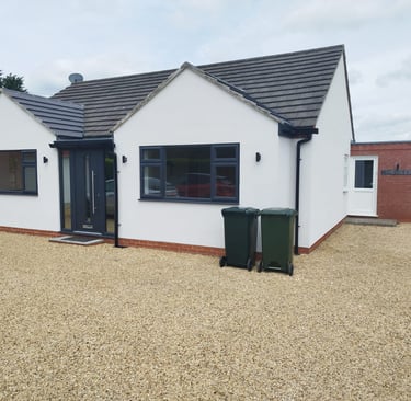 Exterior of a painted-white bungalow, with a black-tiled roof and black detailing.