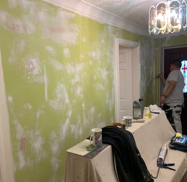 An in-progress entrance hallway, with sheet covered furniture and a painter working on the wall.