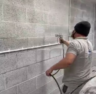 LPAD staff using a paint sprayer on an industrial cinderblock wall.