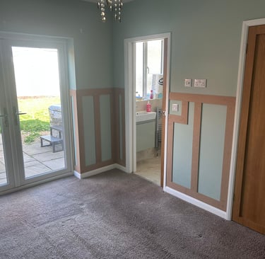 An unfurnished room with grey, painted walls and wooden rectangular detailing on the lower half.