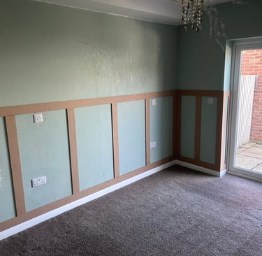 An unfurnished room with grey, painted walls and wooden rectangular detailing on the lower half.