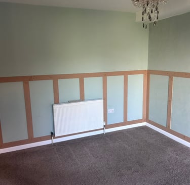 An unfurnished room with grey, painted walls and wooden rectangular detailing on the lower half.