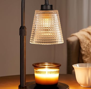 Electric candle warmer lamp with a glass shade melting a scented jar candle on a wooden table.