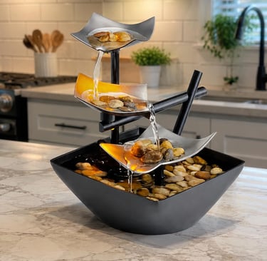 Modern 3-tier tabletop water fountain with river stones on a white marble kitchen countertop.