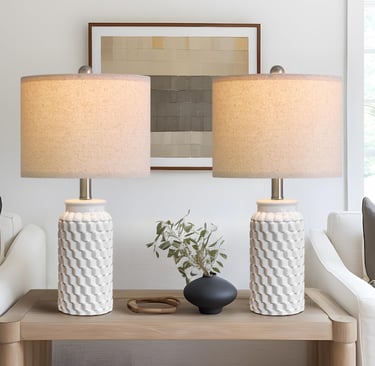 Pair of white textured ceramic table lamps with tan linen shades on a wooden console table.