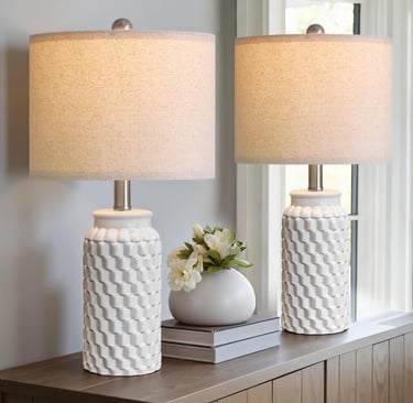 Pair of white ceramic table lamps with a textured honeycomb base and linen shades on a wooden sideboard.