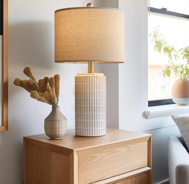 Modern ceramic table lamp with a linen shade on an oak wood nightstand in a bright bedroom.